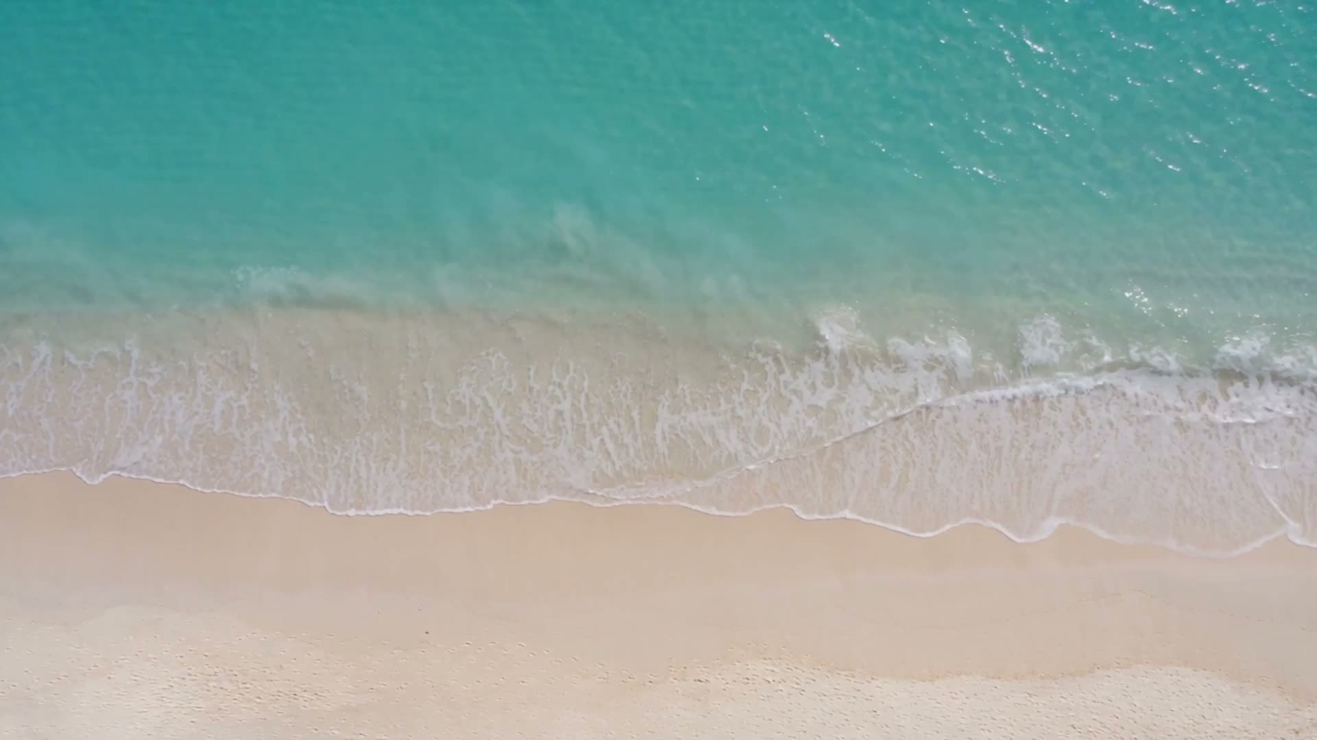 Aerial view of a turquoise sea washing onto a white-sand beach